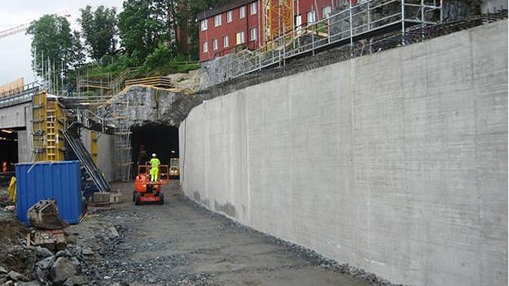 Norra Länken 11 Byggarbetsplats med arbetare och maskiner nära en tunnelentré omgiven av byggnadsställningar.