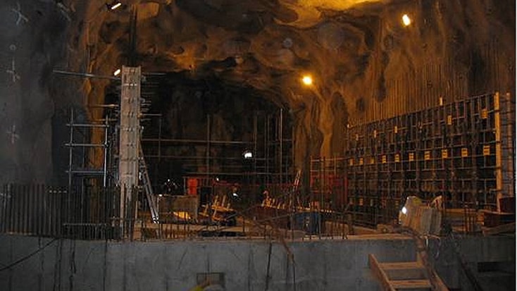 Norra Länken 11 Underjordisk byggarbetsplats med byggnadsställningar, belysning och armerade betongkonstruktioner.