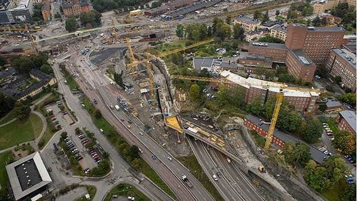 Norra Länken 11 Flygvy över en urban byggarbetsplats med kranar, vägar och angränsande byggnader i en stadsbild.
