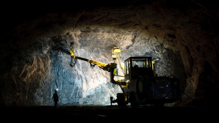 Skanska har anlagt tre bergrum för en ny tunnelbanedepå i Norsborg. Gruvdrift under jord med tung utrustning och en arbetare upplyst i en mörk tunnel.