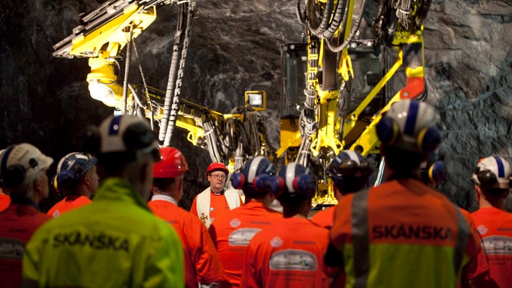 Totalt arbetade omkring 50 personer på platsen. Byggnadsarbetare i säkerhetsutrustning observerar tung maskinering under jord, vilket visar Skanskas projekt.