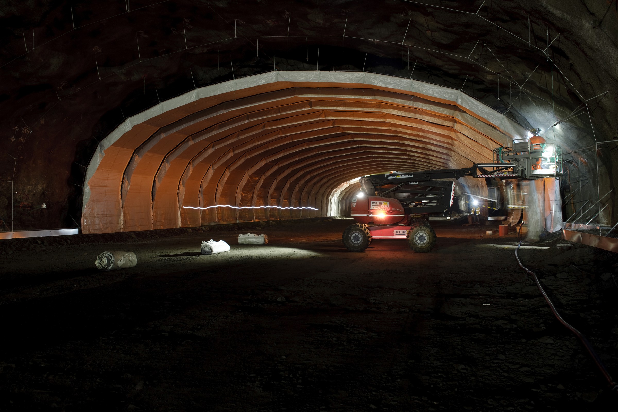 Valet att lägga depån under mark ger stora miljövinster, då inte markytan utnyttjas för anläggningen. Byggutrustning i en svagt upplyst tunnel med synliga bärande stödstrålar.