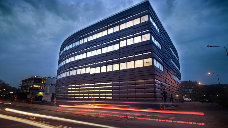 Modern kontorsbyggnad med elegant glasfasad upplyst vid skymningen, som fångar stadens gatuliv.
