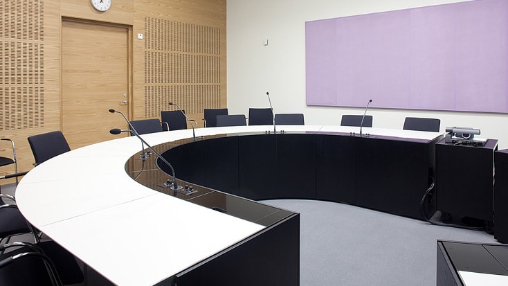 Modernt konferensrum med ett böjt bord, mikrofoner, stolar och en lavendel akustikpanel.
