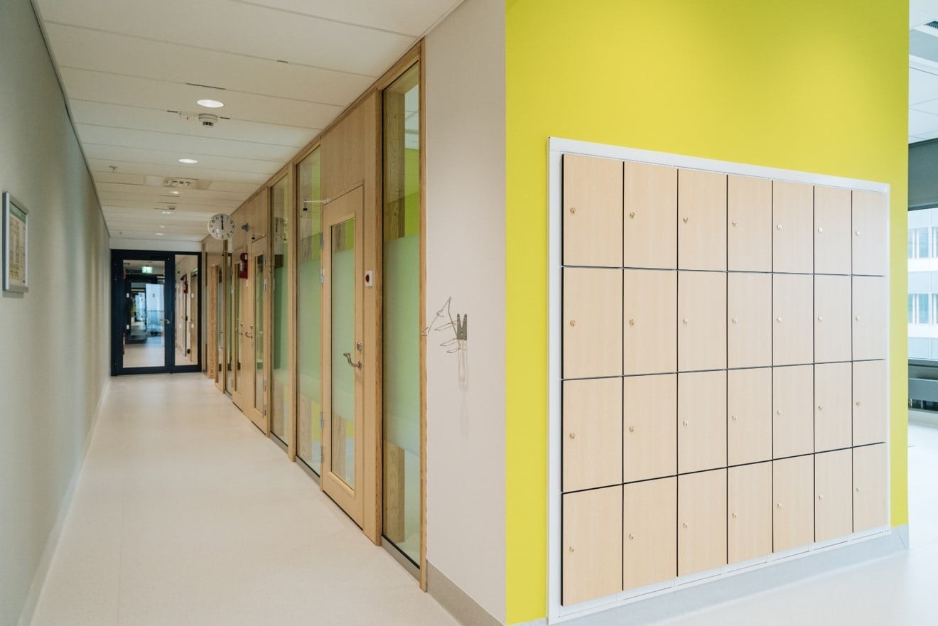 Modern hall med trädörrar, skåp och ljusgul vägg, vilket skapar en livlig interiör.