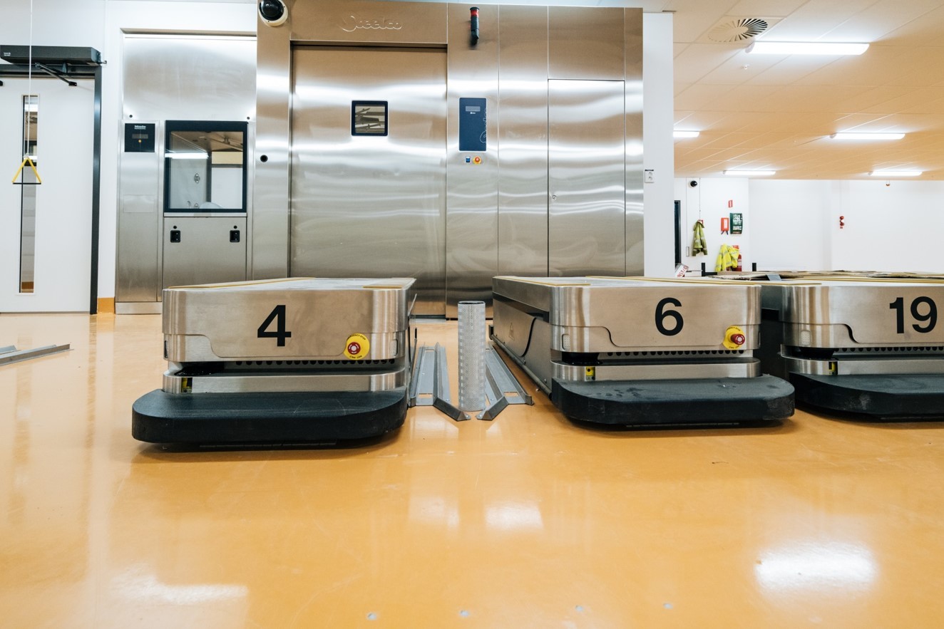 Automatiserade styrda fordon numrerade 4, 6 och 19 i ett lager med industriell utrustning.