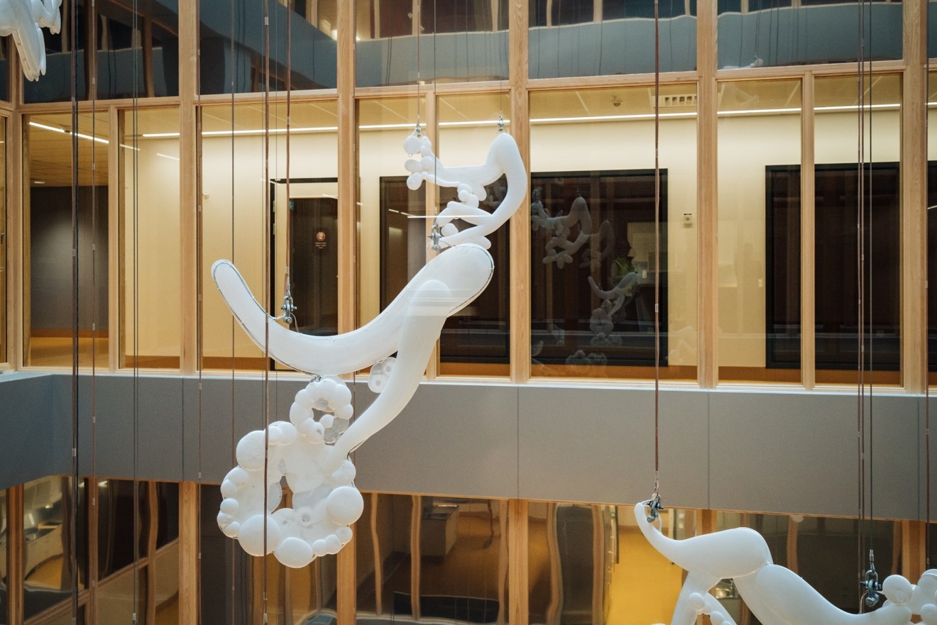 Skulpturala vita ballonger upphängda i ett modernt atrium med trä- och glasarkitektur.