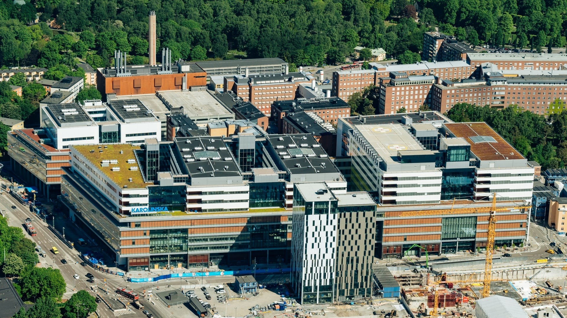 Flygvy över Karolinska Universitetssjukhusets byggnader omgivna av frodig grönska i Stockholm.