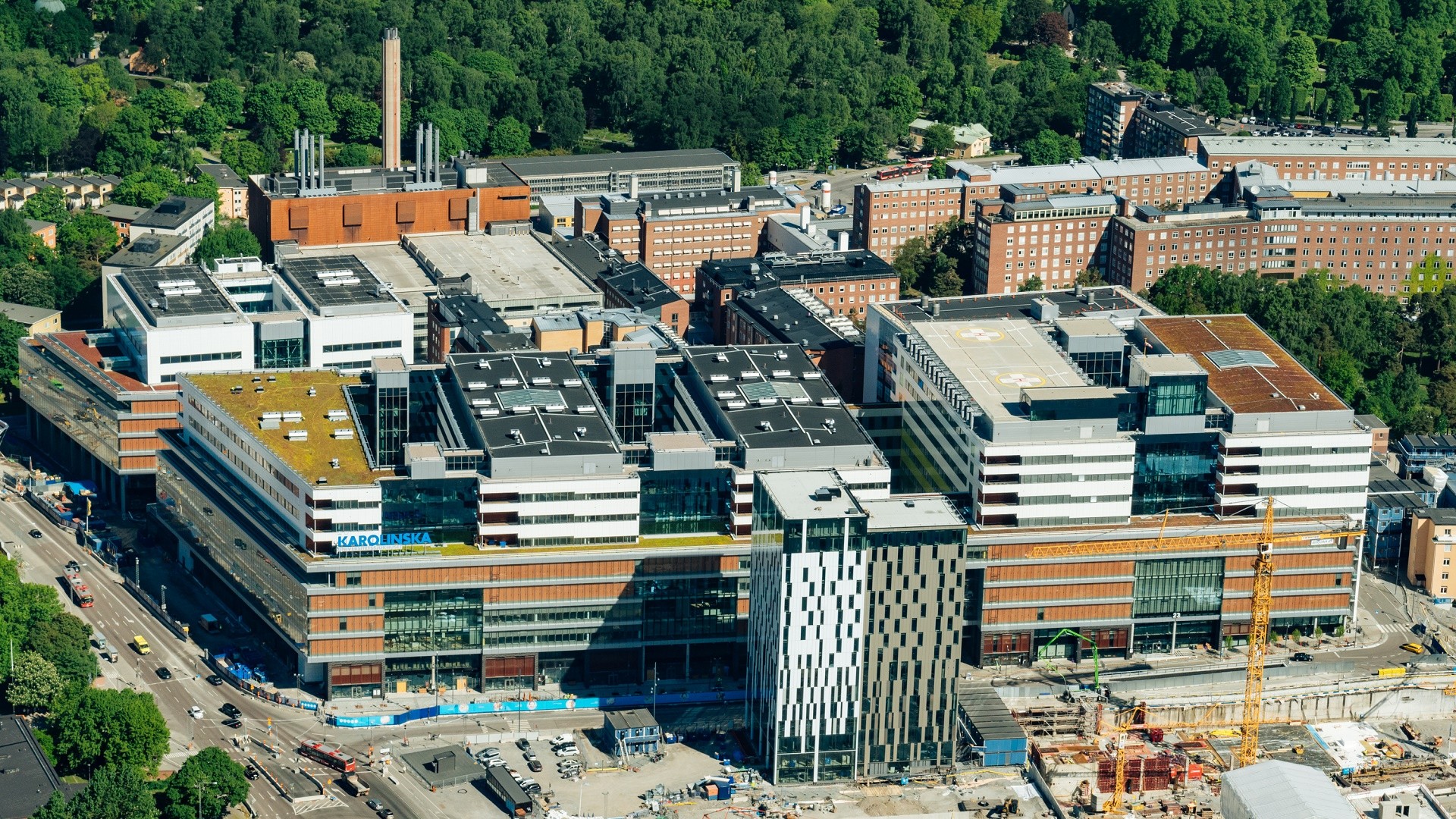 Nya Karolinska Solna, sett från luften. Flygvy över Karolinska Universitetssjukhusets byggnader omgivna av frodig grönska i Stockholm.