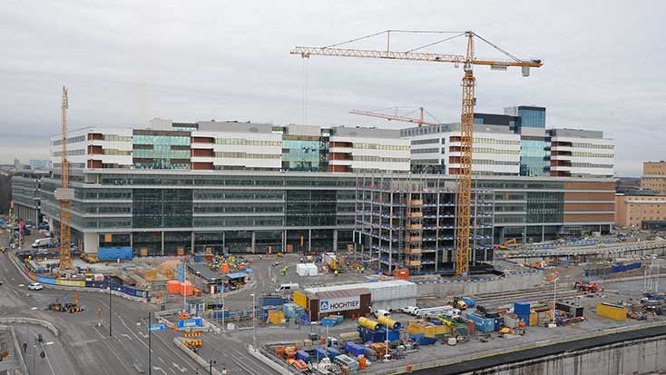 Byggarbetsplats med kranar och moderna byggnader, med glasfasader och urban infrastruktur.