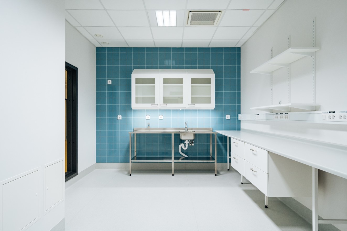Modern laboratorierum med blå kaklad vägg, vita skåp och enhet med rostfri diskho.