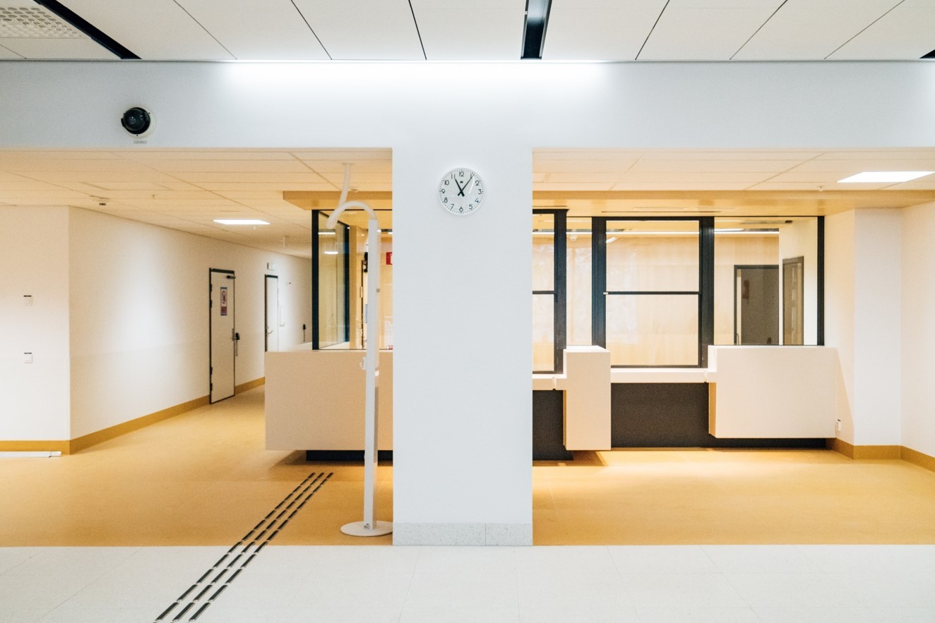 Modern sjukhusreception med beige golv, vita väggar och en väggmonterad klocka som visar 7:10.