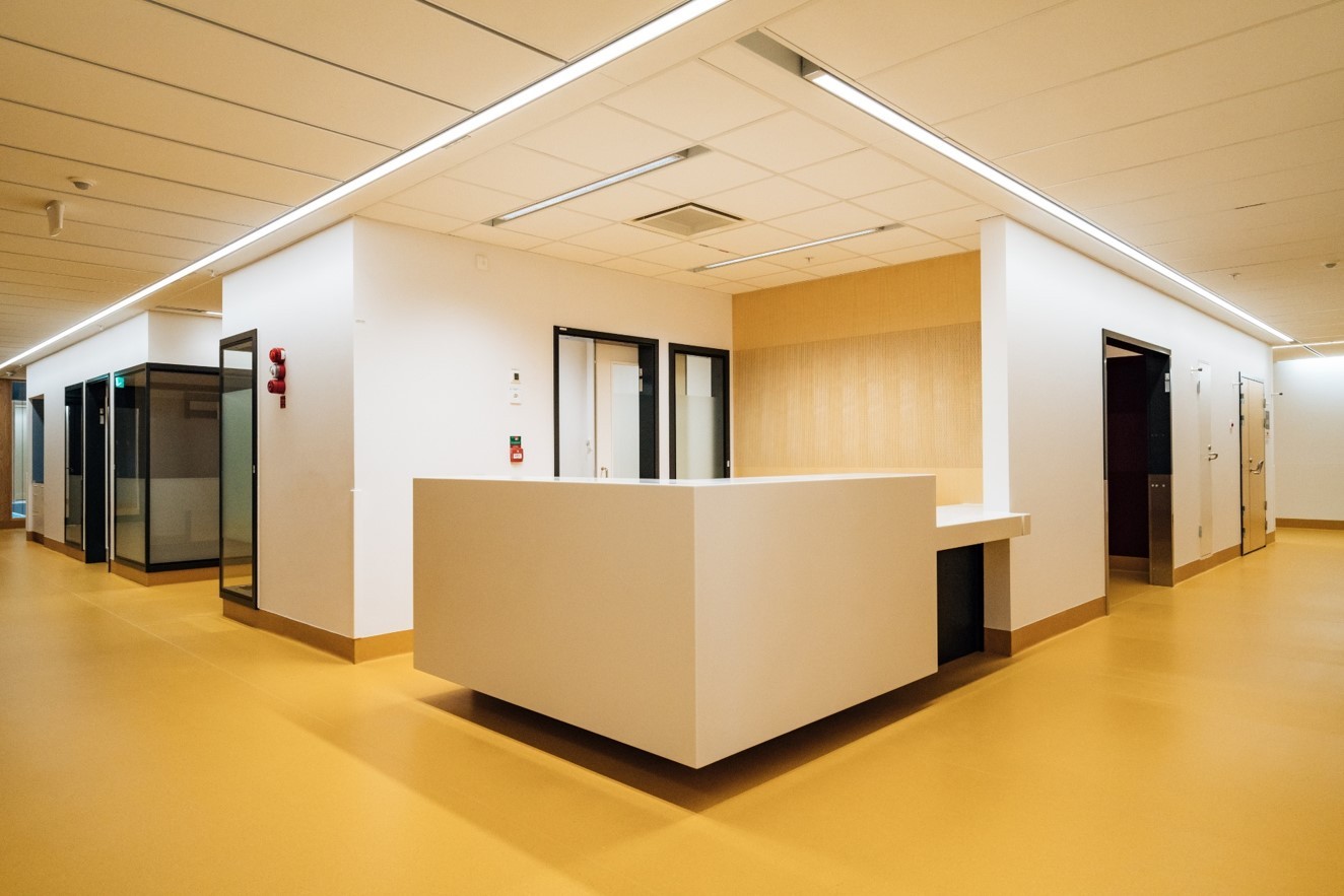 Modern sjukhuskorridor med en central reception, stark belysning och beige golv.