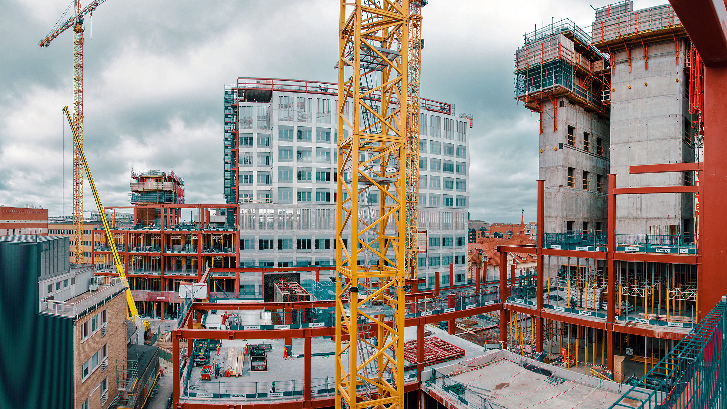 Stadsbyggnadsplats med kranar och delvis byggda strukturer under en molnig himmel.
