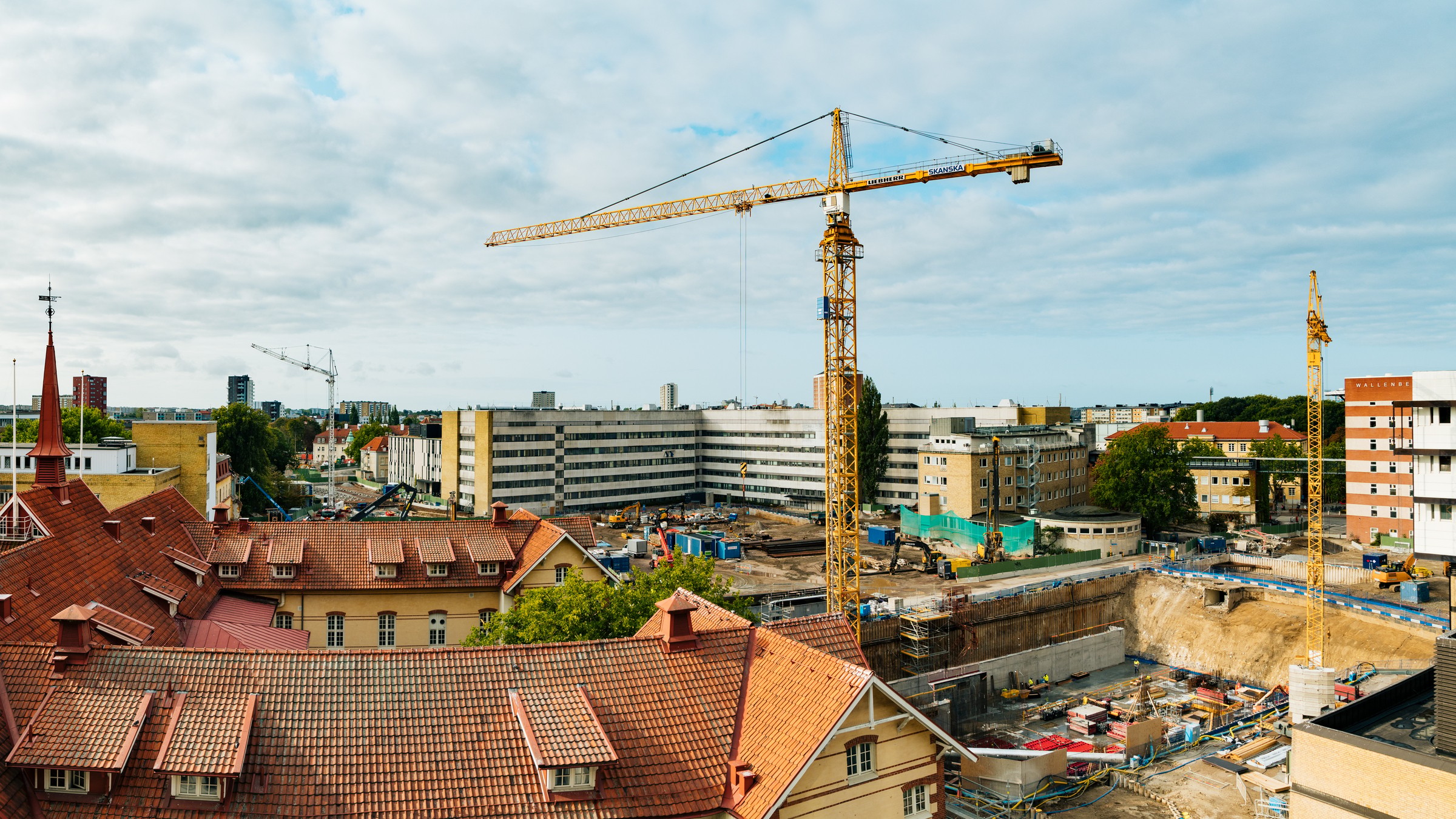 Byggarbetsplats med kranar och byggnader under utveckling, omgiven av urban arkitektur.