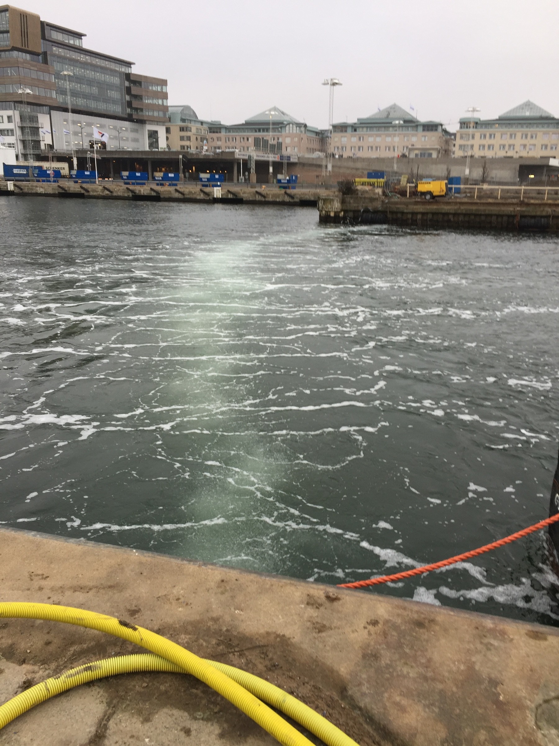 För att sänka grumlingsvärdet har vi monterat en så kallad bubbelledning. Hamnmiljö med skummande vatten, rep och industribyggnader i bakgrunden.
