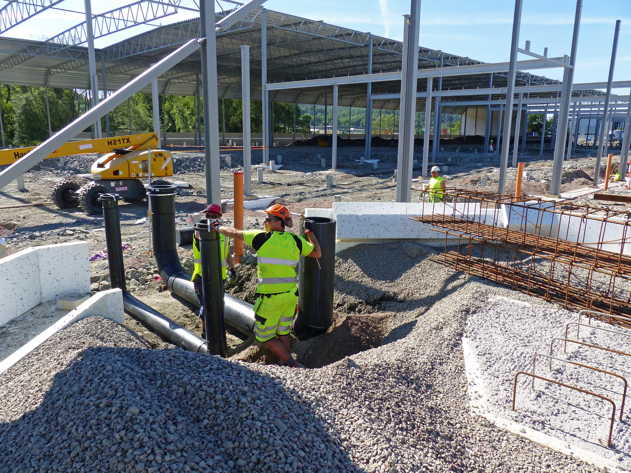 Byggprocessen gick snabbt efter grundläggningsarbetet. Byggnadsarbetare installerar dräneringsrör på en industriplats med strukturella stålramar.