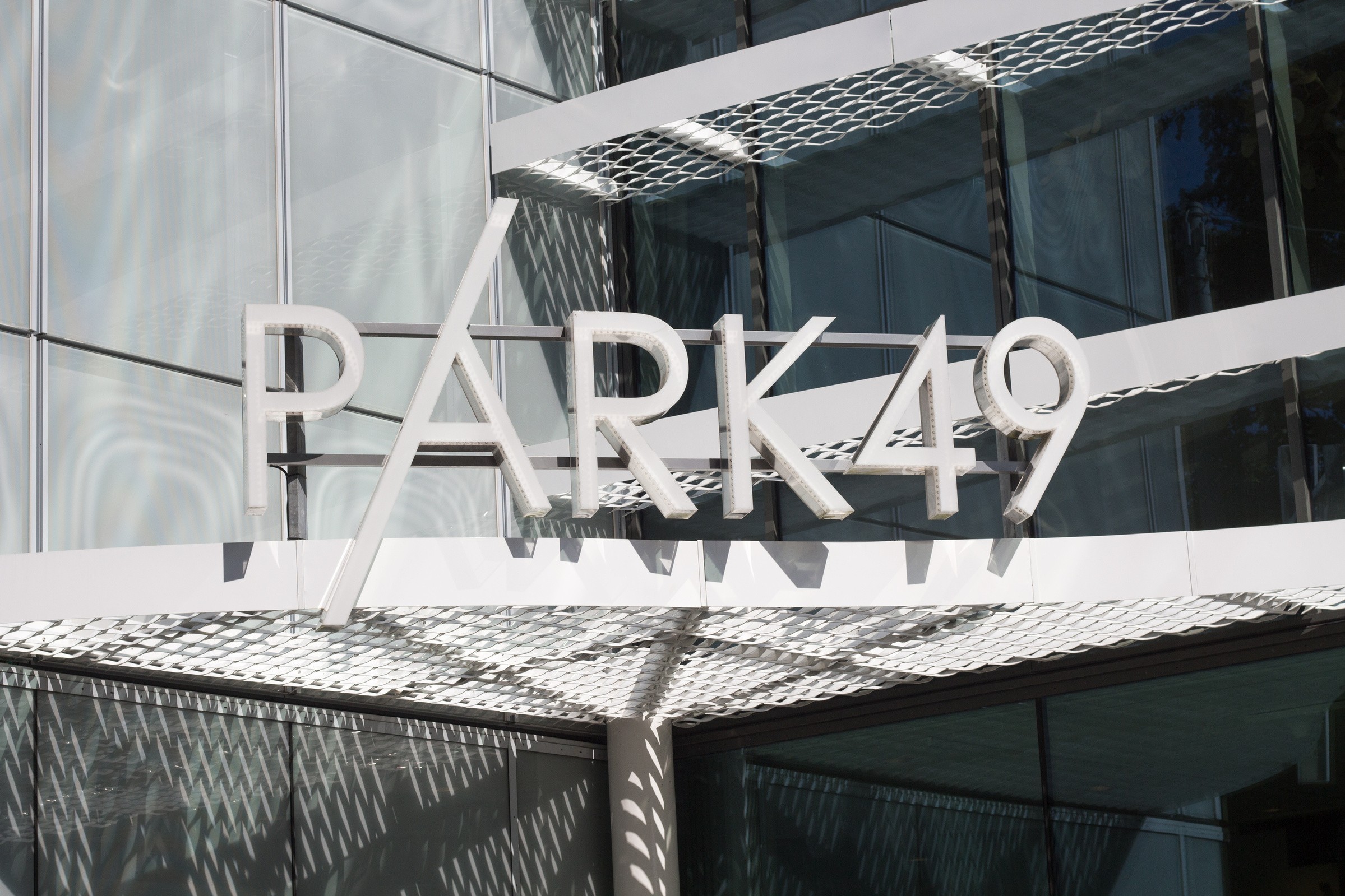 Skyltning med "PARK49" på en modern byggnadsfasad med glas- och metallelement.