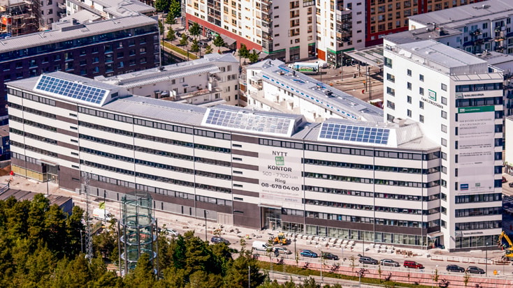Sjöstadsporten Modern kontorsbyggnad med solpaneler på taket, omgiven av stadsmiljö i dagsljus.