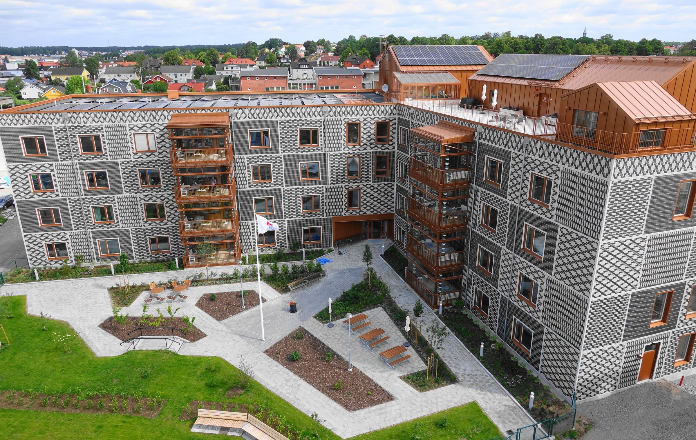 Modern lägenhetsbyggnad med mönstrad fasad, solpaneler, balkonger och anlagd innergård.