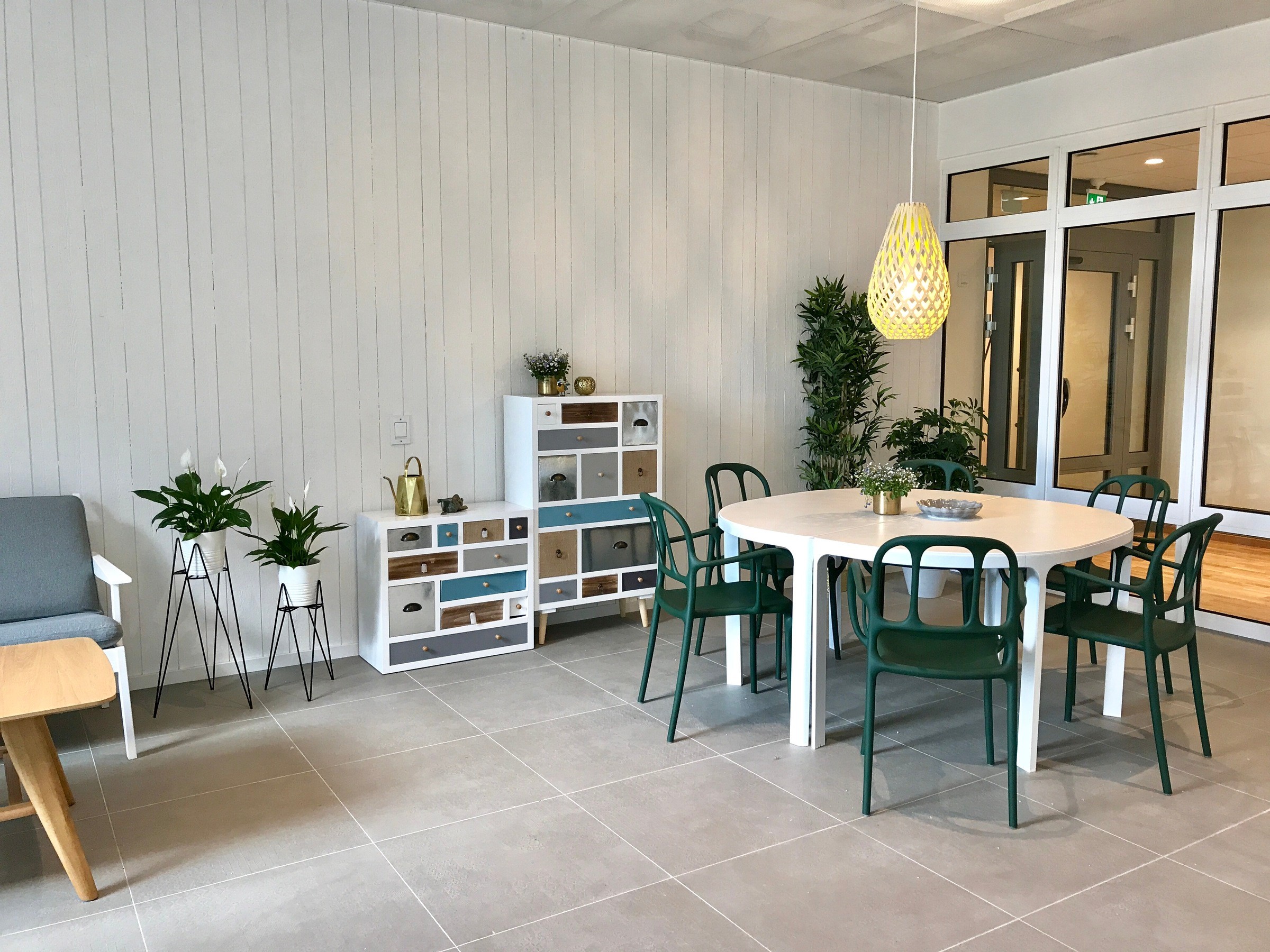 Modern matplats med gröna stolar, runt bord, inomhusväxter och dekorativa hyllor.