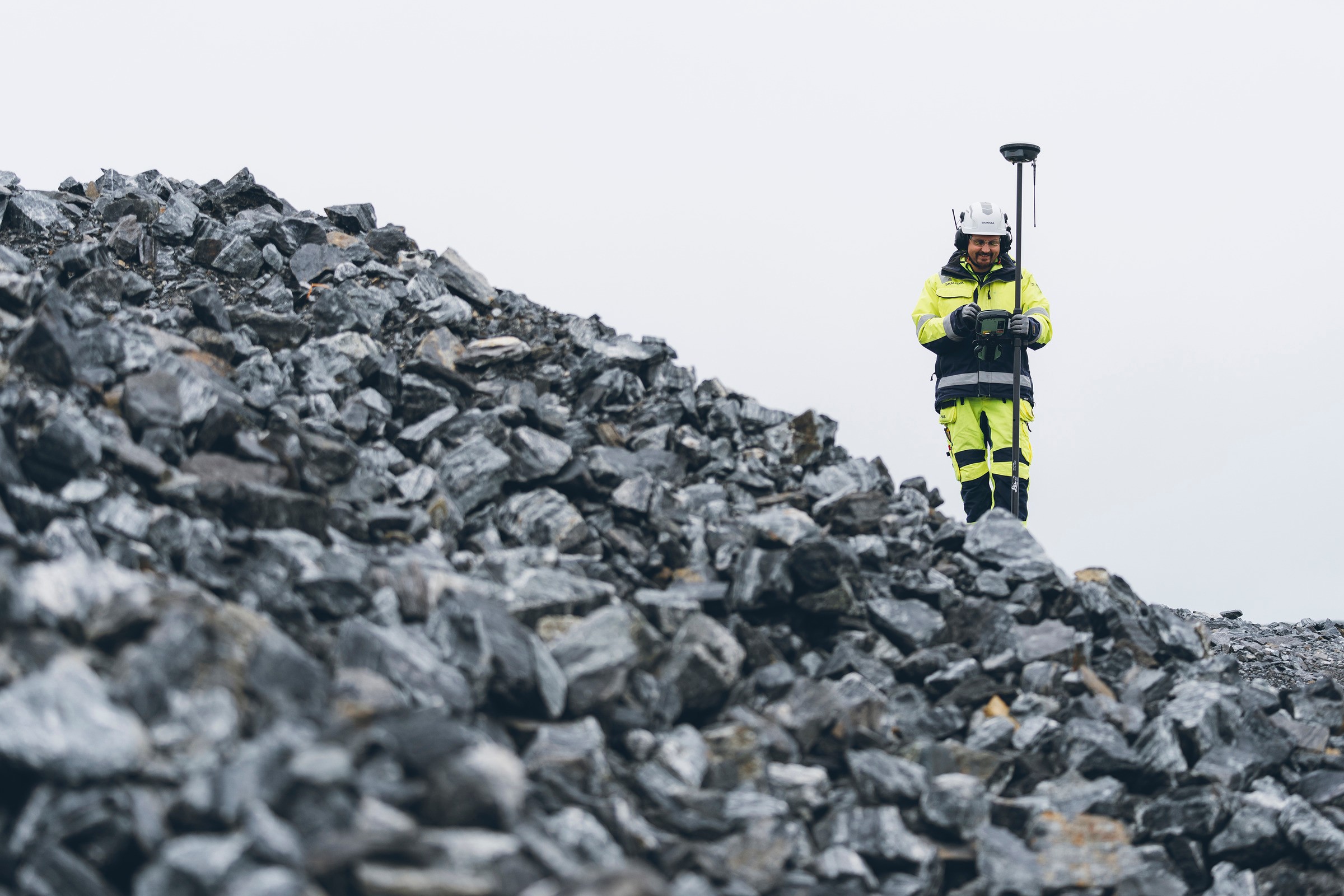 Surveyor i högsynlighetsutrustning mäter terräng med GPS-utrustning på stenig landskap.