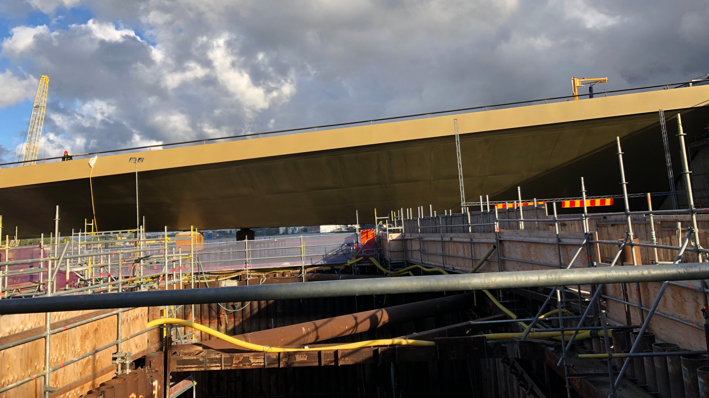 Bron sedd från arbetsplatsen. Byggarbetsplats med byggnadsställningar och en stor brokonstruktion under en molnig himmel.