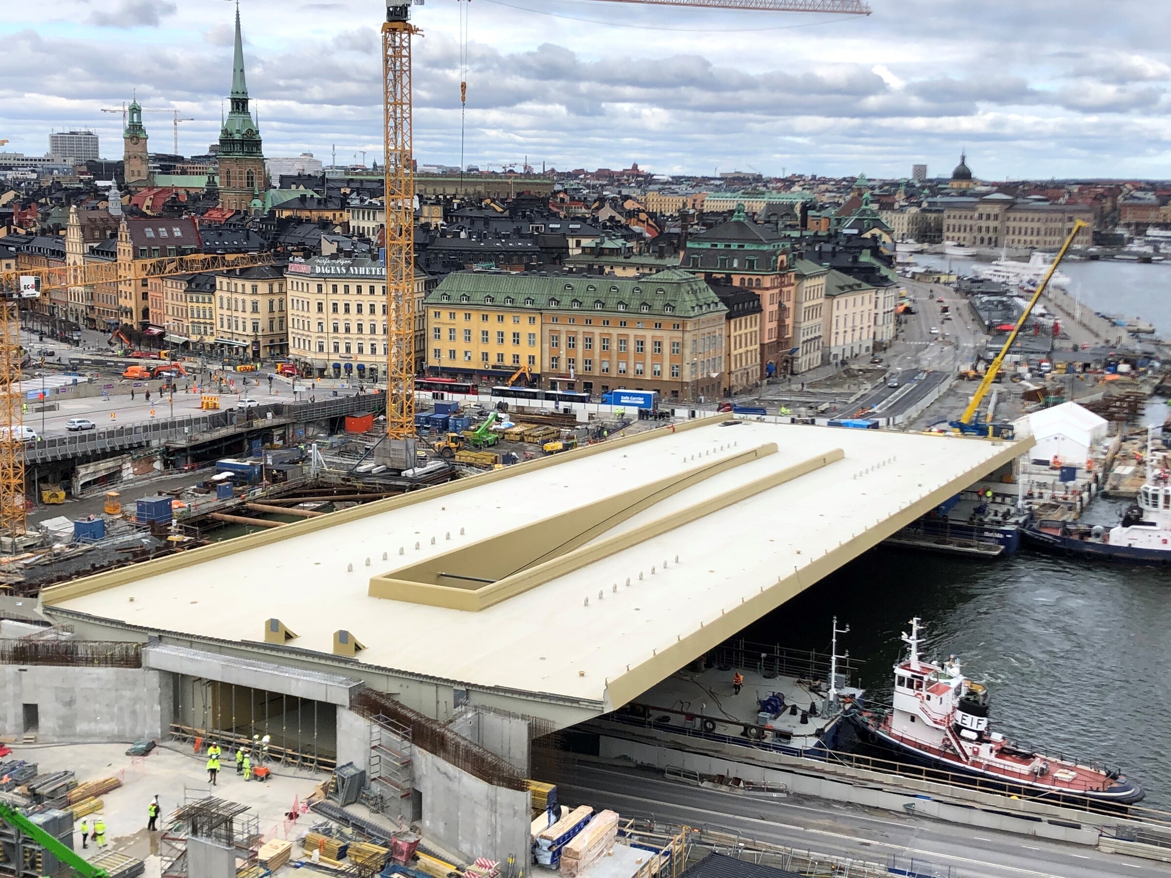 Den gyllene bron är på plats med 10 millimeters marginal. Byggandet av en stor bro över vatten i ett stadsområde med synliga kranar och arbetare.