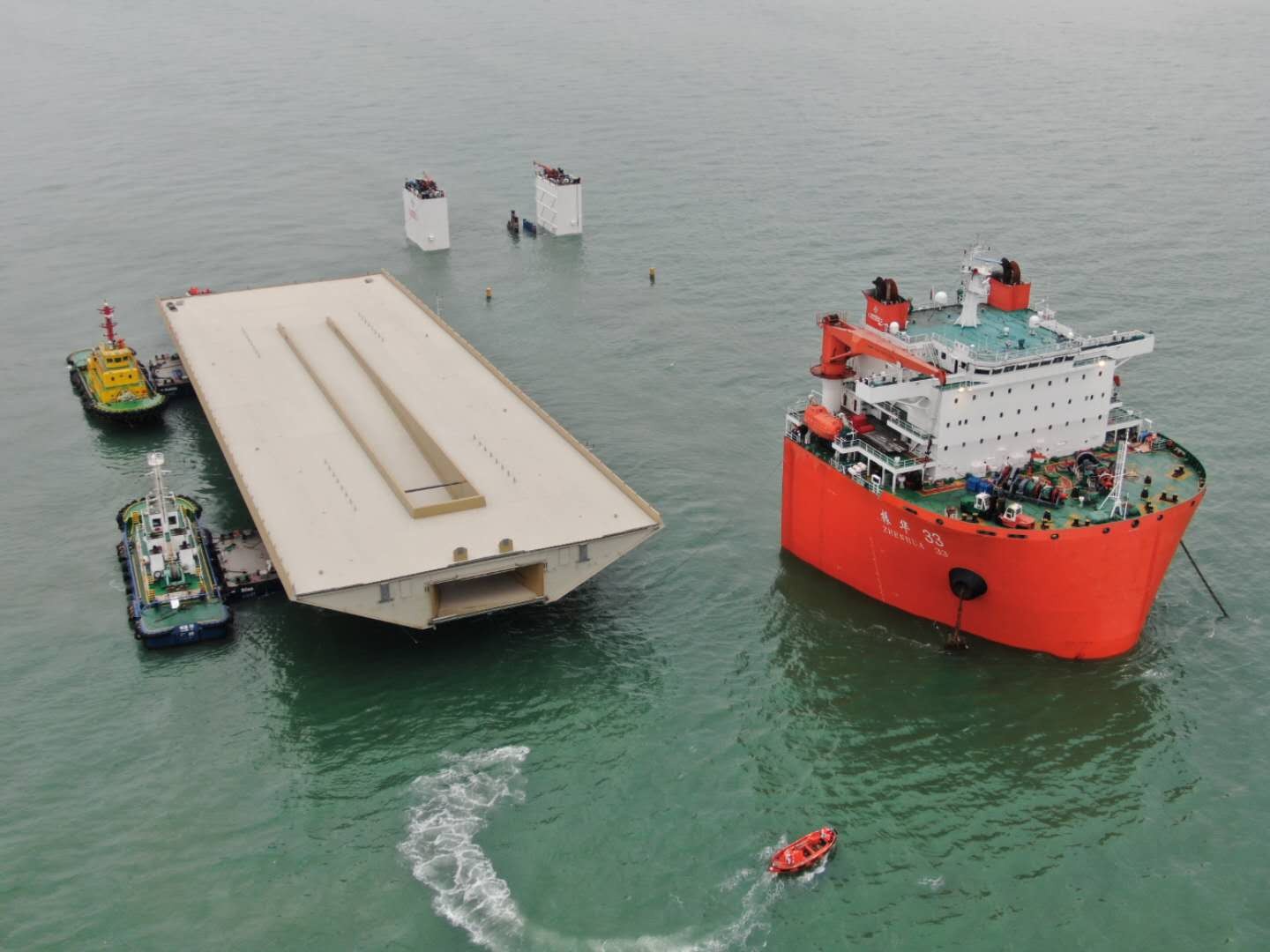 Pontonerna med bron flöts in på ett nedsänkbart skepp, ett så kallat semi-submersible transport ship som sedan tar hela bron över havet till Stockholm. Källa för bilder: Foster+Partners Perry Ip Stort fartyg och bogserbåtar styr en massiv brosektion mot stödpelare i havet.