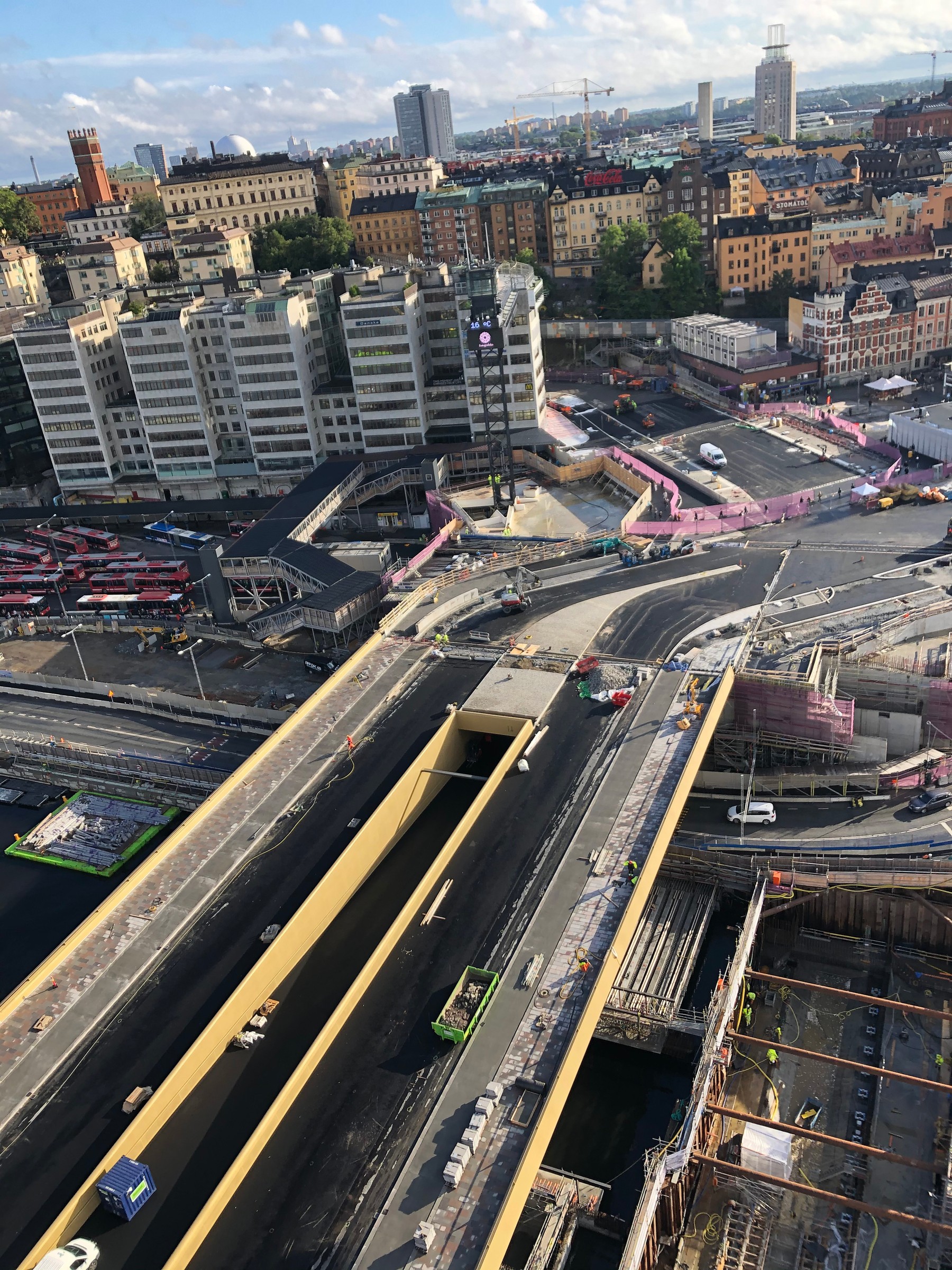 Slussbron sedd från kranen. Flygvy över en urban byggarbetsplats med vägar, byggnader och kranar i bakgrunden.