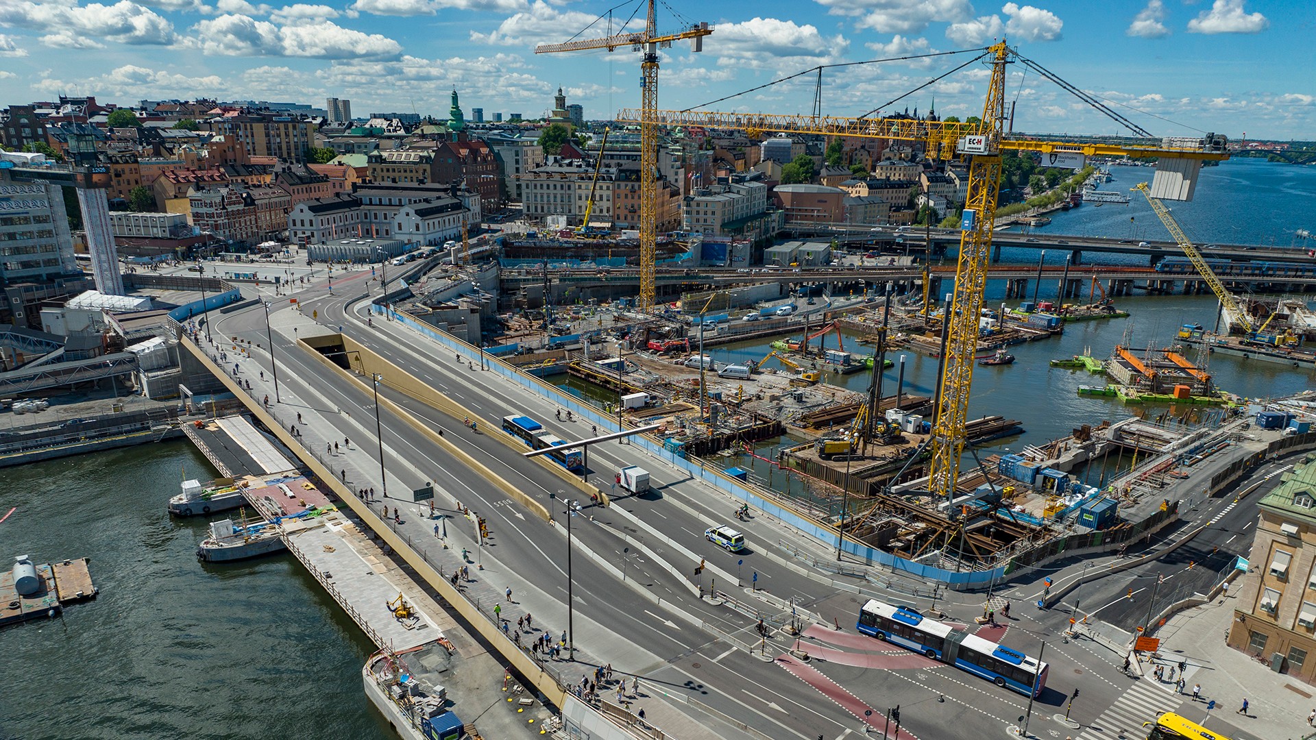 Slussbron, Skeppsbrokajen och östra lågbron. Här pågår markarbeten för öppning av lågbron mot slutet av året. Foto Lennart Johansson, Stockholms stad. Slussen från ovan med bussar som trafikerar bron och byggkranar i Saltsjön intill.