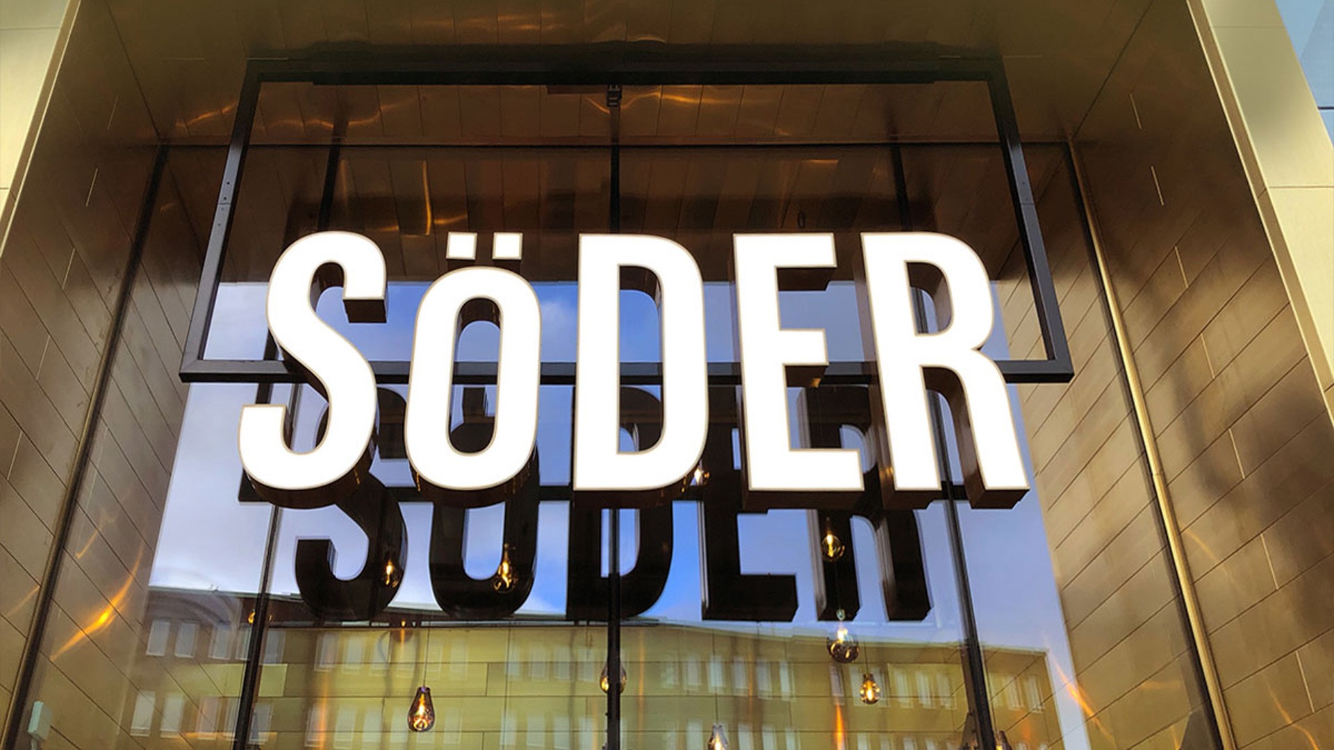 Söderpunktens entré till gallerian. Skylt med texten "SÖDER" i feta vita bokstäver mot en reflekterande glasfasad.