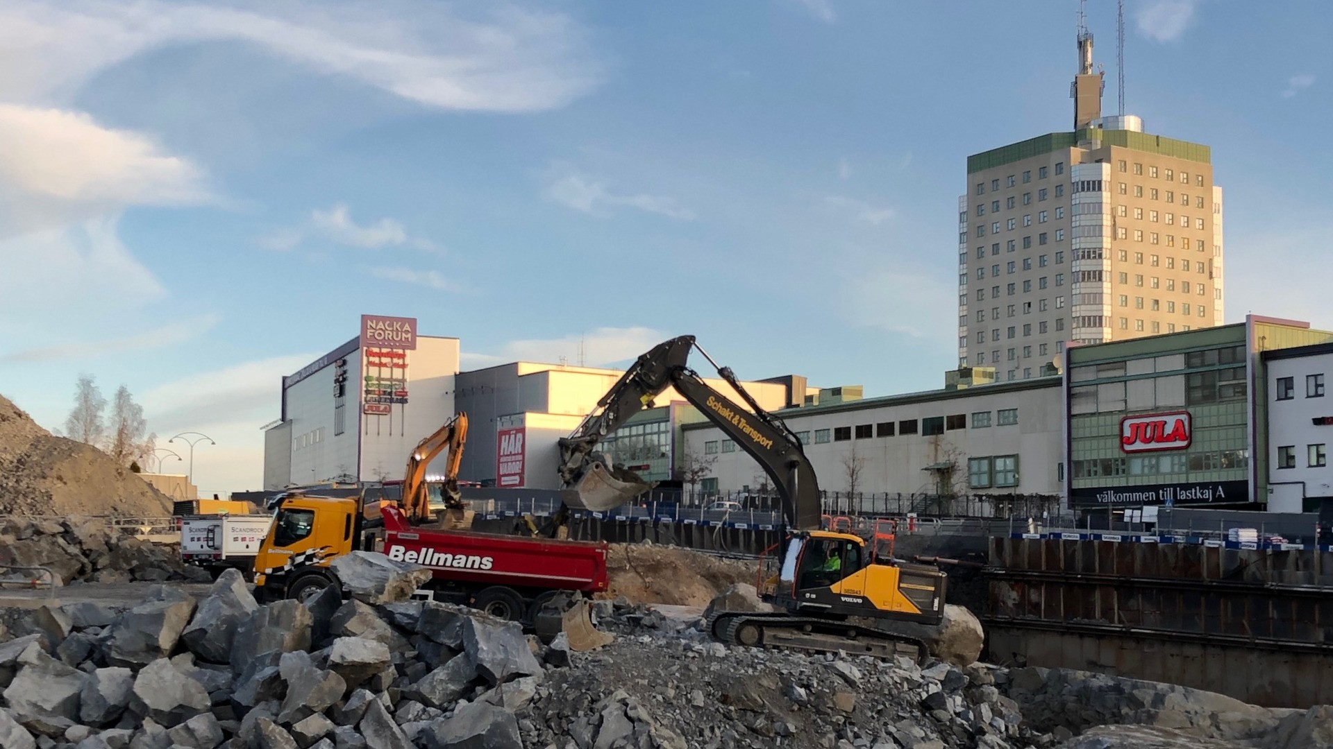 Skanska bygger vägar, torgytor, vatten- och avloppsledningar längs Värmdövägen som går mellan Sickla och Nacka Forum. En grävskopa som lastar på en lastbil.