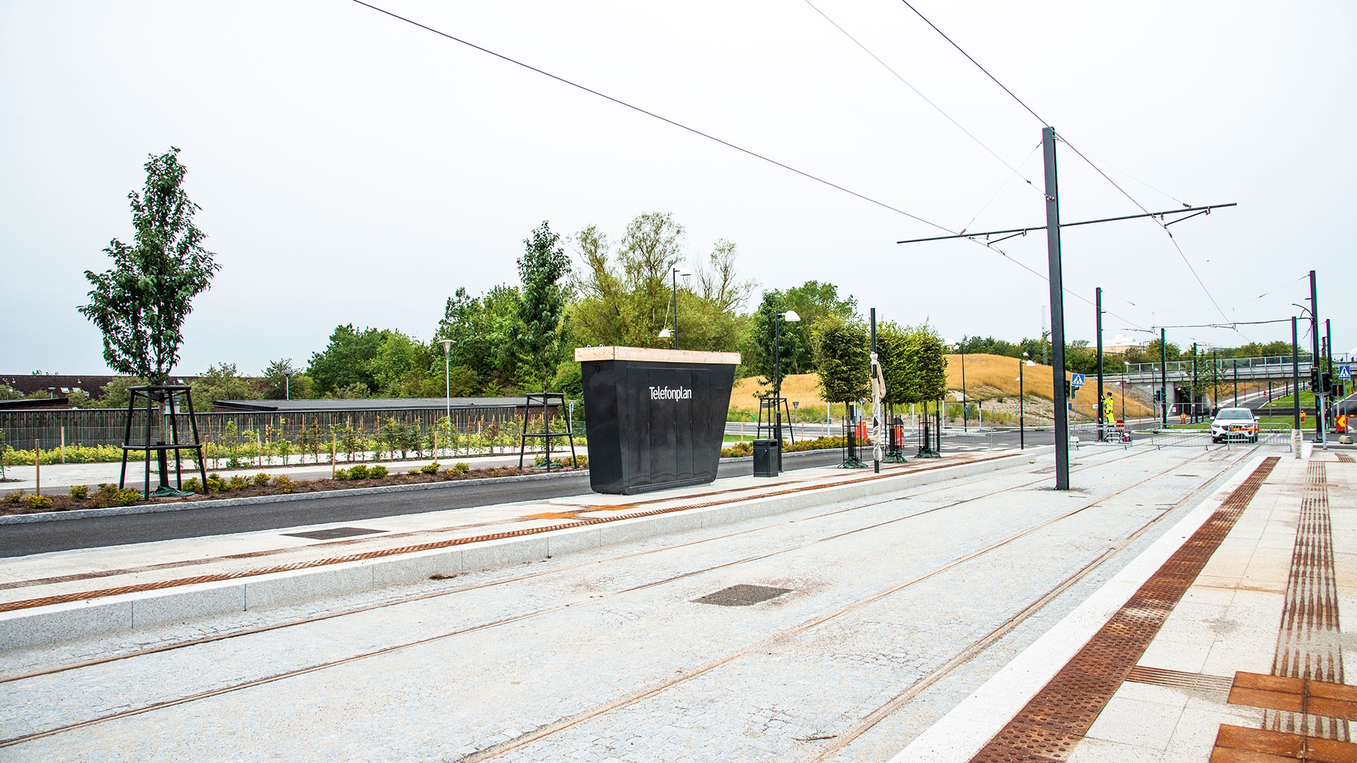 Modern spårvagnsstation med spår, träd och en skylt som lyder "Nobelplein" under en klar himmel.