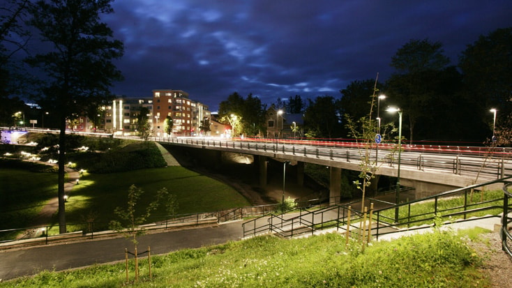 S:t Larsbron Nattvy av en väl upplyst bro över en anlagd park, med stadens byggnader i bakgrunden.