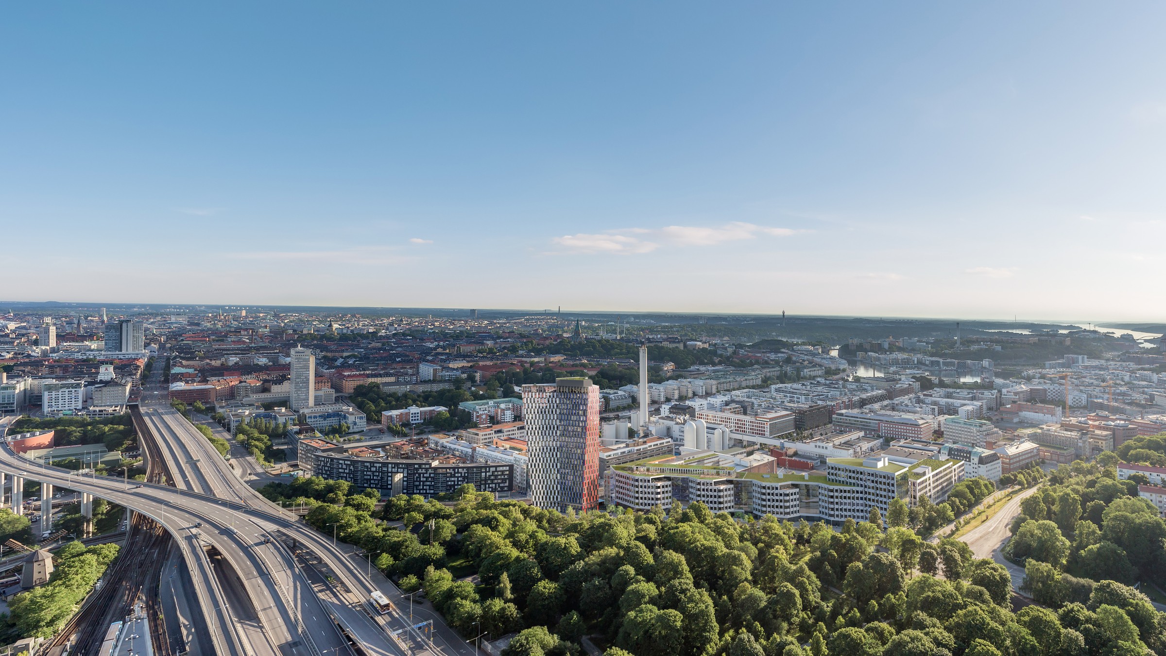 Flygvy över Stockholm med stadsmiljö, framträdande skyskrapor och frodig grönska.