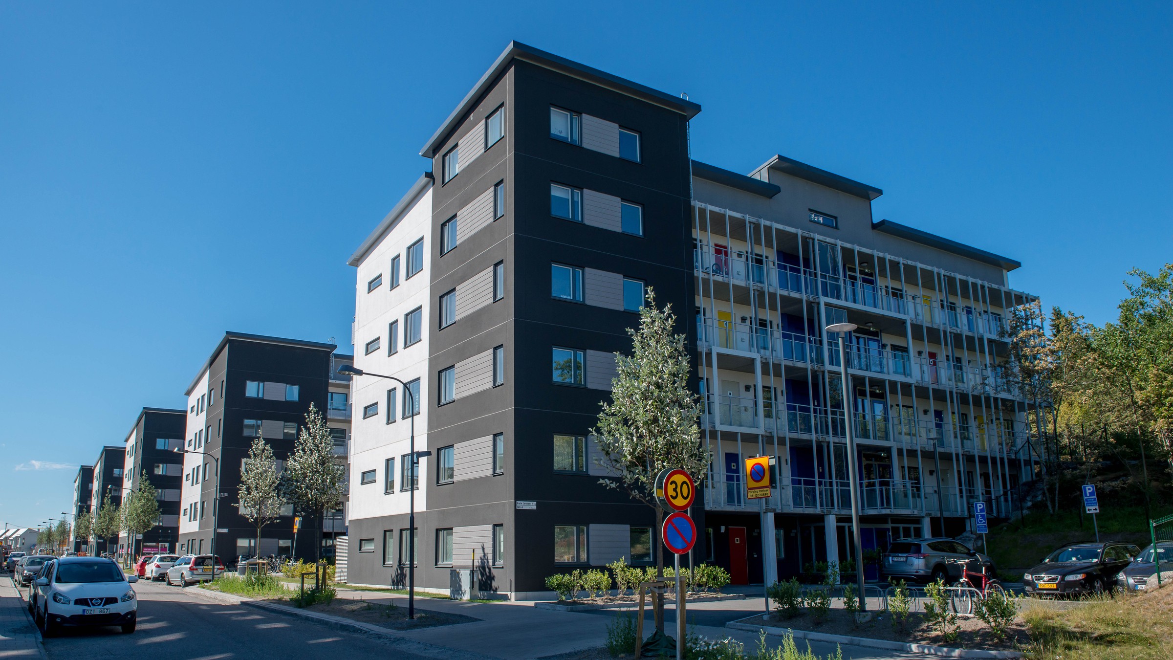Modernt flerbostadshus med parkering och gatutecken under en klar blå himmel.