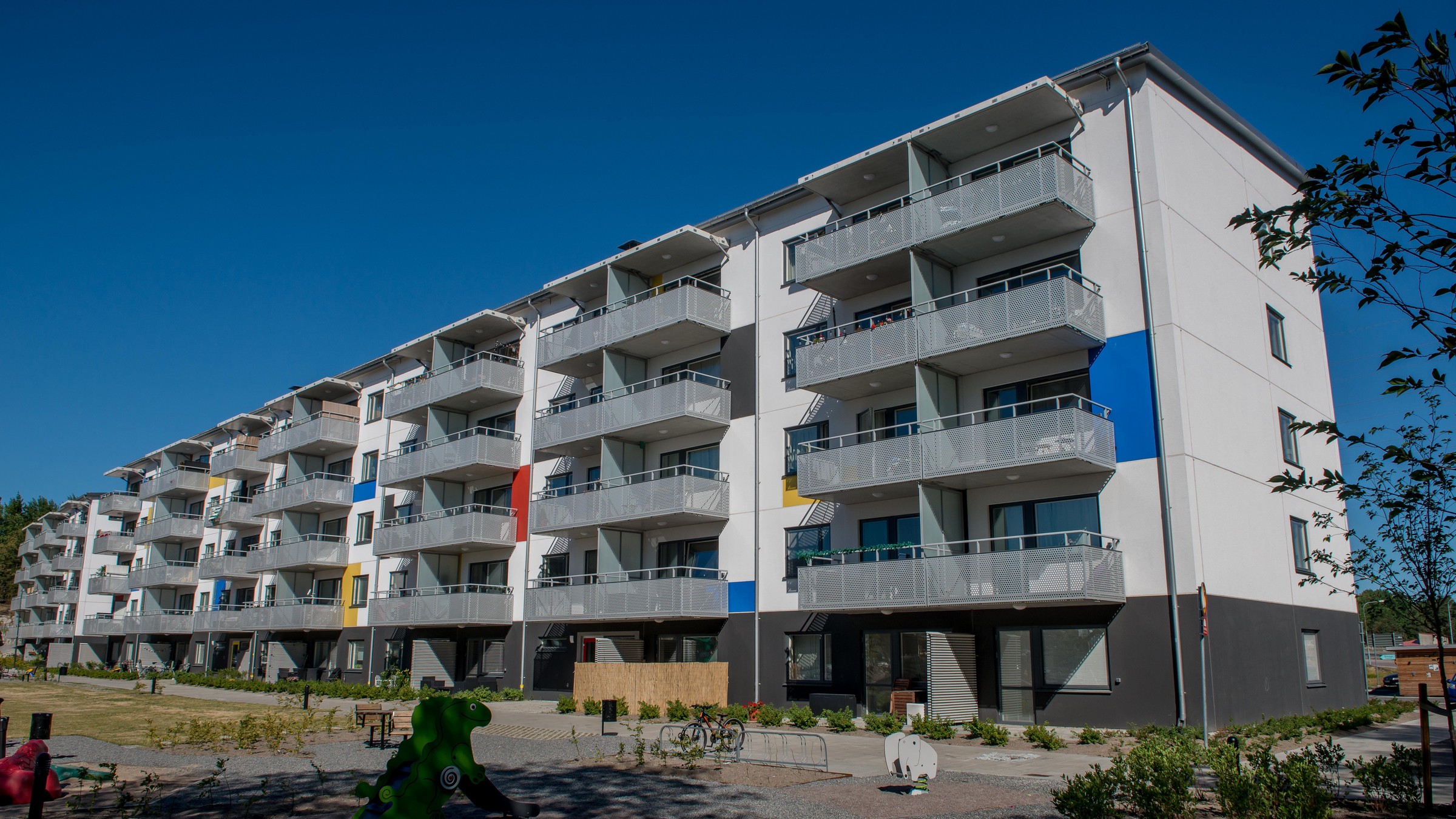 Modern lägenhetsbyggnad med färgglada accenter och balkonger i ett soligt bostadsområde.