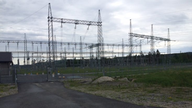 Elektrisk kraftstation med högspänningsmaster och ledningar mot en bakgrund av molnig himmel.