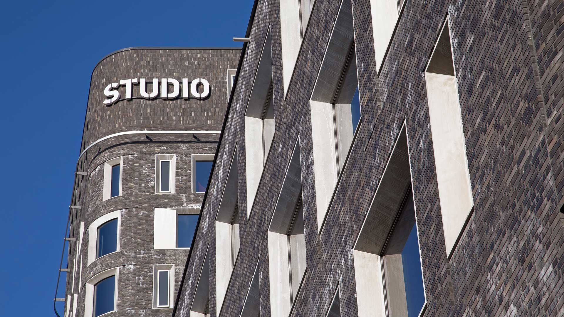 Fasad logga Modern byggnad med "STUDIO"-skylt, med tegelvägg och geometrisk fönsterdesign.
