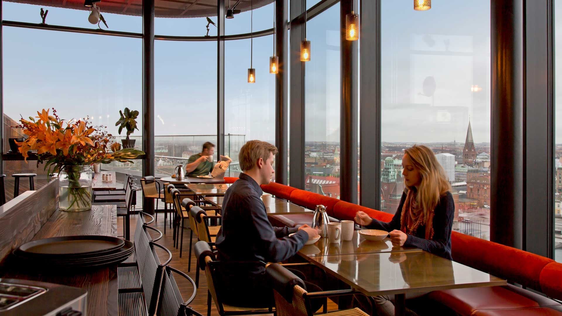 Skybar Ett par njuter av kaffe i ett modernt café med stora fönster som erbjuder utsikt över stadens silhuett.