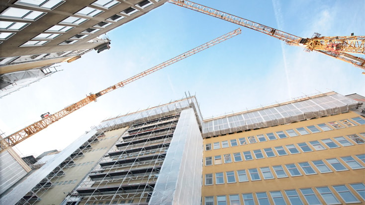 Byggnader under konstruktion med kranar och byggnadsställningar mot en klarblå himmel.