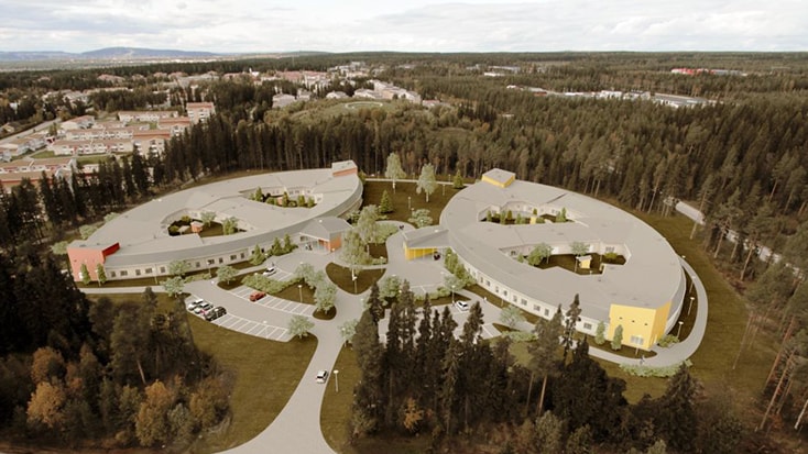 Flygvy över moderna, cirkulära byggnader omgivna av skog och ett parkeringsområde.