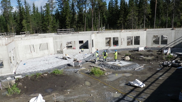 Byggarbetsplats med arbetare som bygger en betongstruktur mitt i en skogsklädd bakgrund.