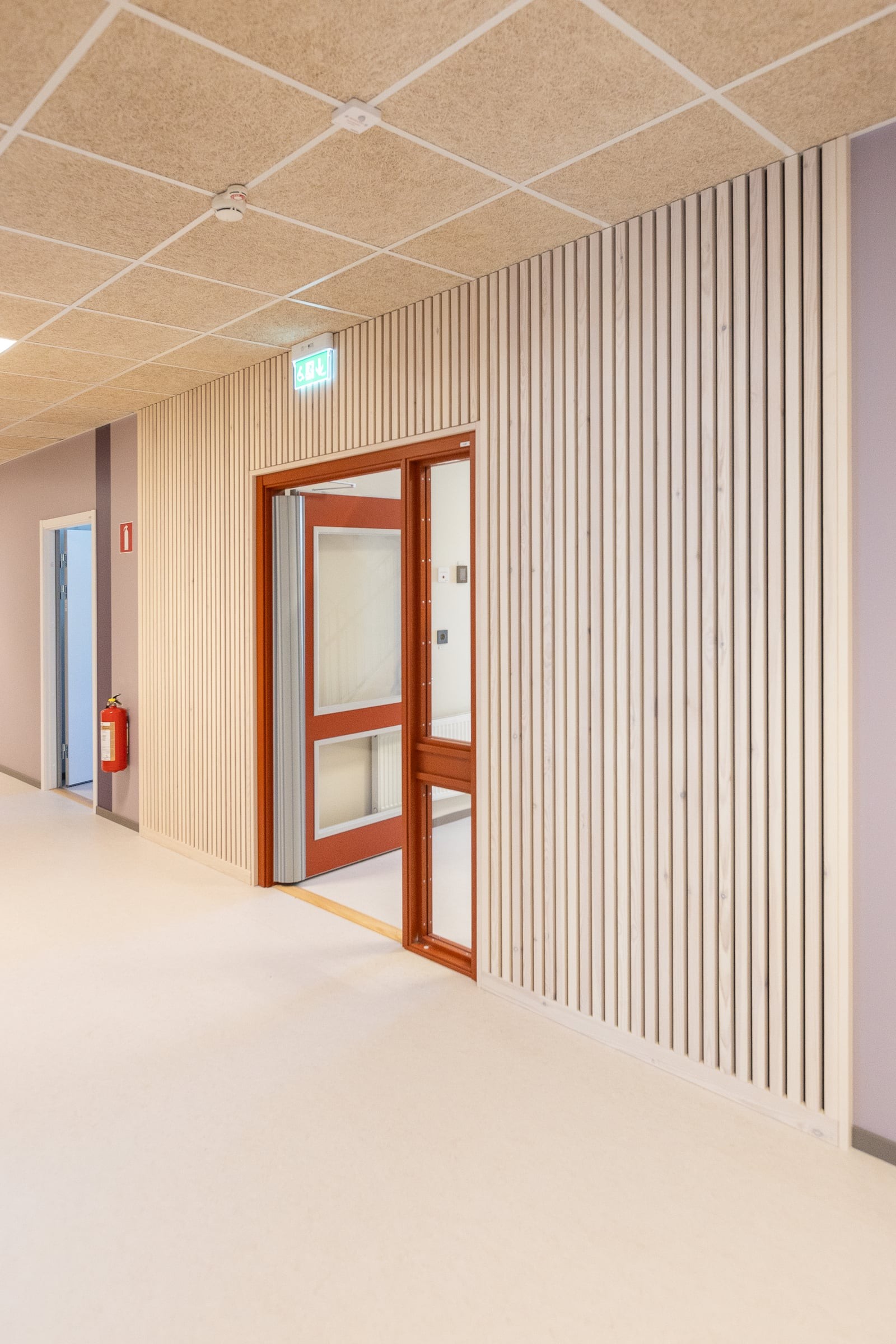 Korridor i Västerängsskolan med väggpanel i trä och dörrar i rödbrunt trä, som skapar en varm och trivsam miljö.