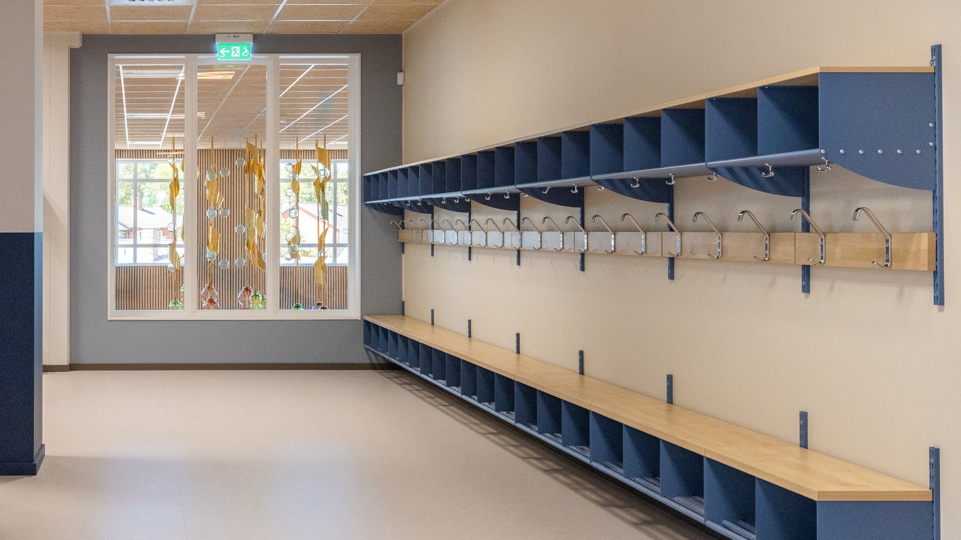 Korridor med blå förvaringshyllor och konstnärlig glasinstallation i fönstret.