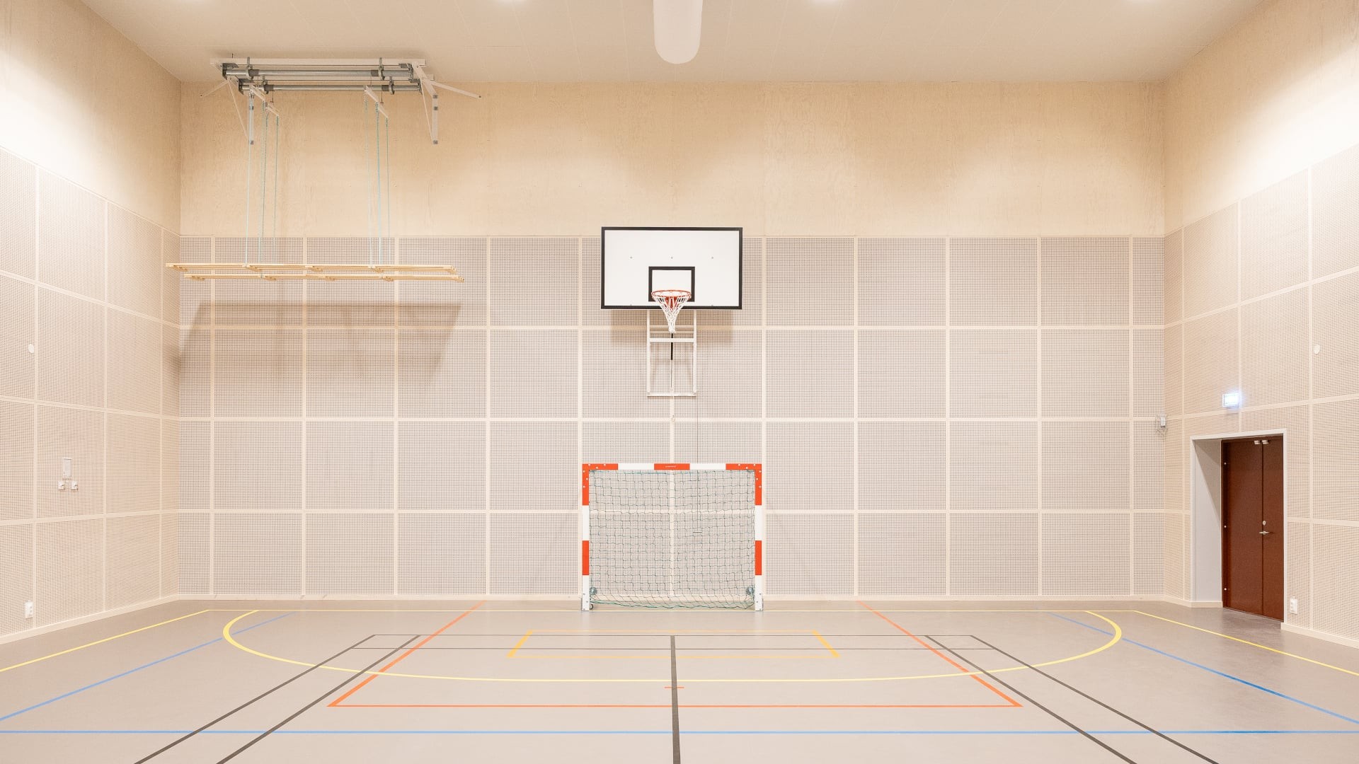 Invändig bild av Västerängsskolans idrottshall med basketkorg, mål och markerad plan.