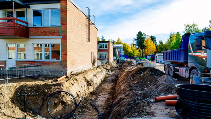 Byggarbetsplats med schaktarbete bredvid en tegelbyggnad, med en lastbil och rör.