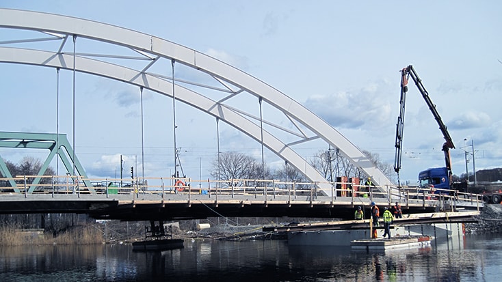 Gemenskapen och viljan att samarbeta har genomsyrat hela projektet. Arbetare bygger en modern bågbro över en flod med kranar och byggnadsställningar på plats.