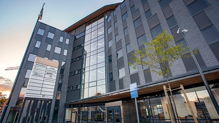 Modern kontorsbyggnad med glasfasad, flera våningar och skyltar som visar företagsnamn.